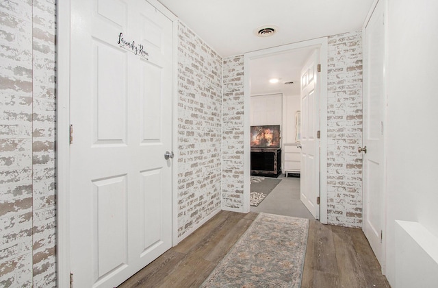 hallway featuring visible vents, wallpapered walls, and wood finished floors