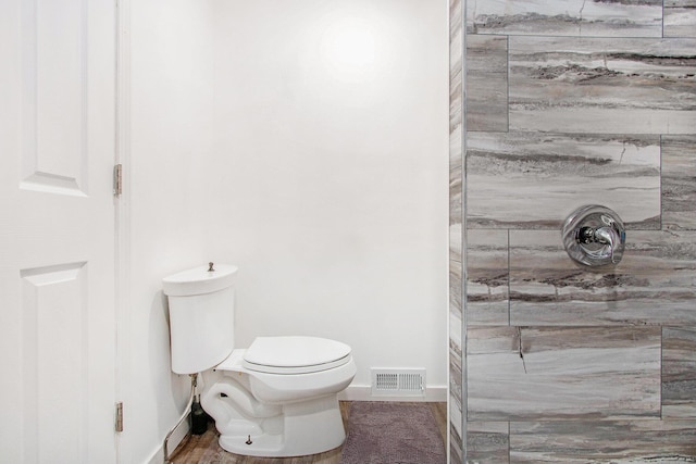 bathroom with visible vents, toilet, tiled shower, and baseboards