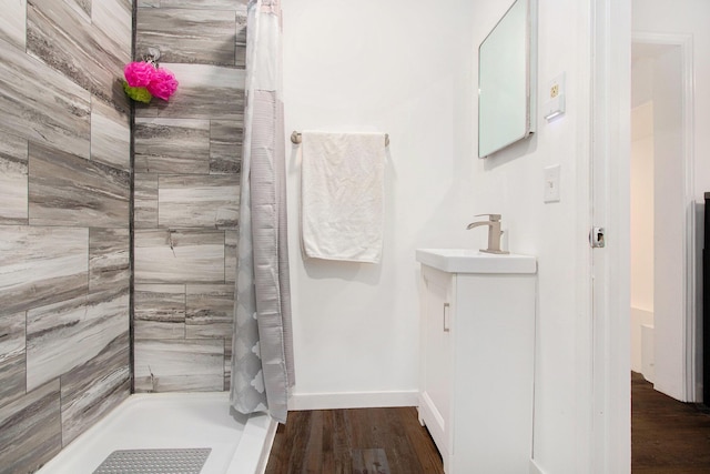 bathroom with tiled shower, vanity, baseboards, and wood finished floors