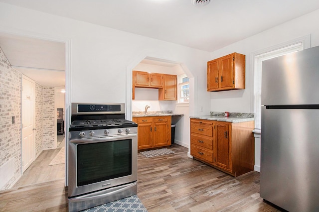 kitchen with brown cabinetry, appliances with stainless steel finishes, light wood finished floors, and a sink