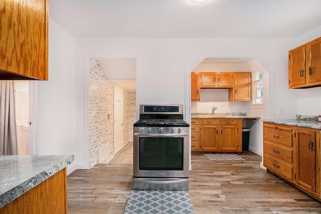 kitchen featuring a sink, brown cabinetry, light wood finished floors, and gas range
