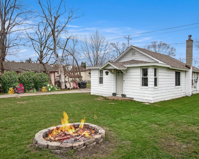 back of house featuring a yard, an outdoor fire pit, a shingled roof, and a chimney
