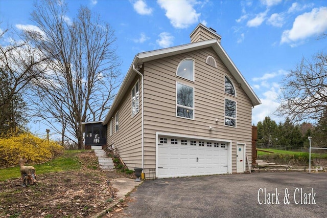 view of property exterior featuring an attached garage, a chimney, aphalt driveway, and fence