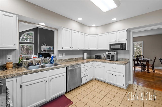 kitchen with black microwave, dishwasher, a sink, and white cabinetry