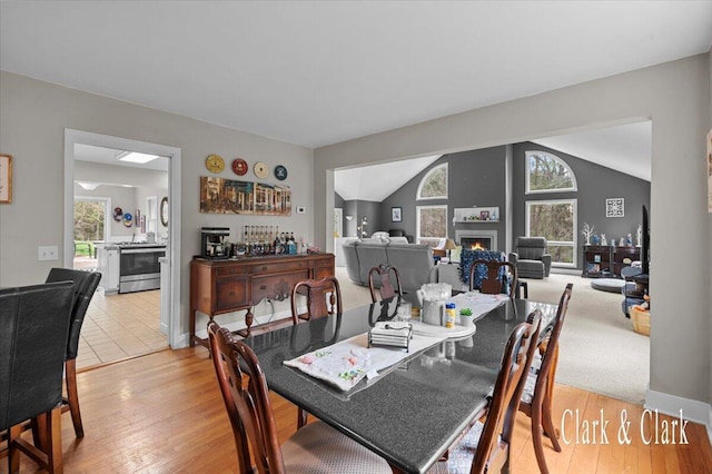 dining area with lofted ceiling, plenty of natural light, light wood-style floors, and a lit fireplace
