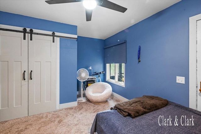 bedroom with carpet flooring, a barn door, baseboards, a ceiling fan, and a closet