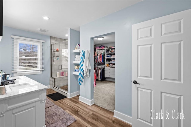 full bathroom featuring recessed lighting, wood finished floors, vanity, a walk in closet, and a stall shower