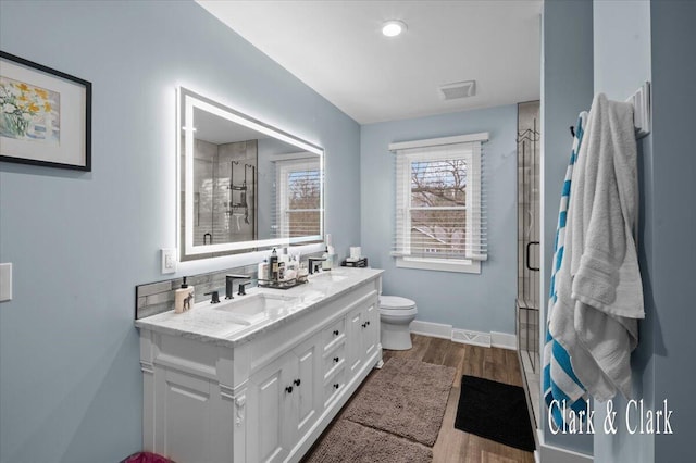 full bathroom featuring a shower stall, wood finished floors, a sink, double vanity, and visible vents
