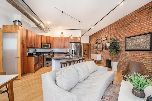 living area with brick wall, light wood-type flooring, and track lighting