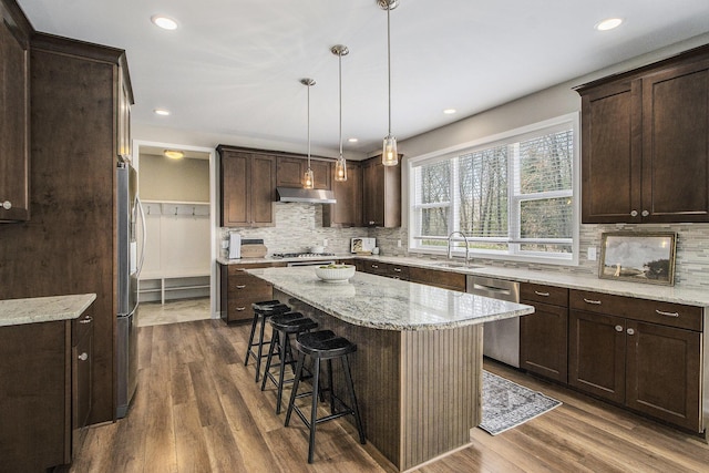 kitchen featuring under cabinet range hood, backsplash, appliances with stainless steel finishes, and a breakfast bar