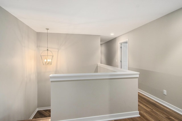 hall featuring baseboards, dark wood-style floors, an upstairs landing, and a notable chandelier