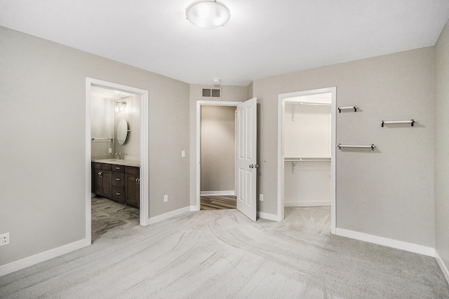 unfurnished bedroom featuring a closet, a spacious closet, visible vents, light carpet, and baseboards