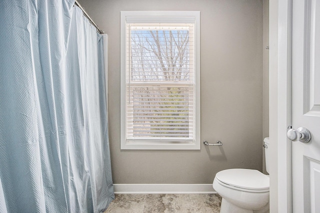 bathroom featuring toilet, baseboards, and a healthy amount of sunlight