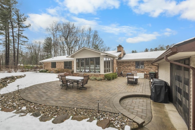 snow covered patio featuring outdoor dining area, a sunroom, and a grill