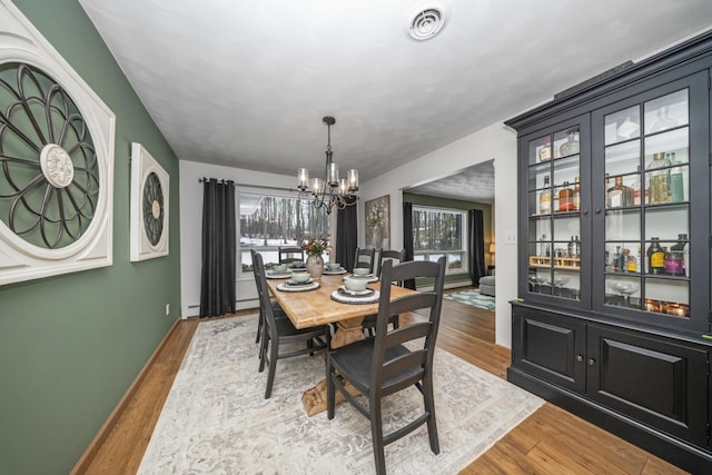 dining area featuring a baseboard radiator, a notable chandelier, wood finished floors, and visible vents