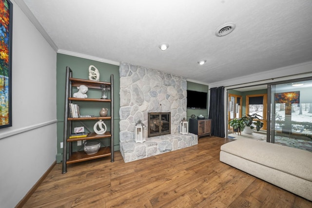 living area with a stone fireplace, visible vents, wood finished floors, crown molding, and baseboards