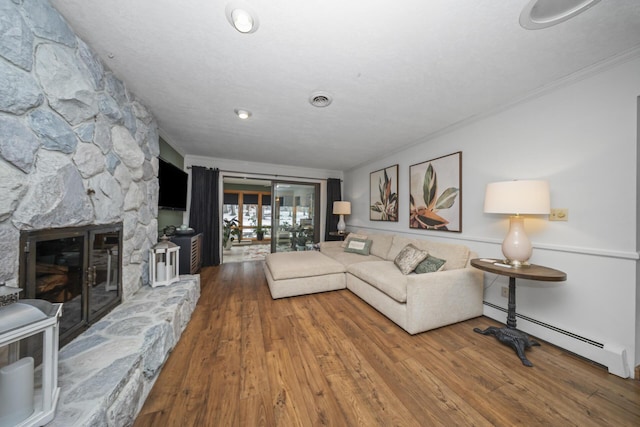 living area with a baseboard radiator, wood finished floors, a fireplace, and ornamental molding