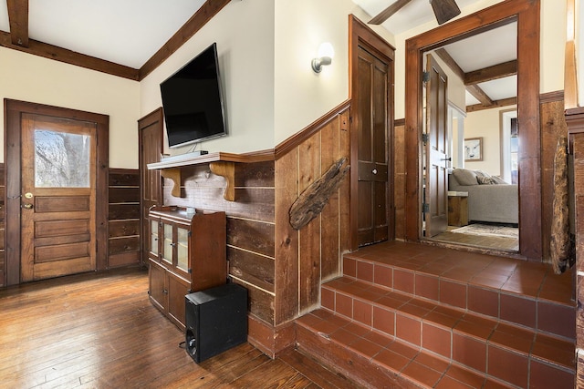 interior space with beamed ceiling, wood walls, dark wood-style floors, and wainscoting
