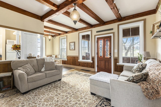living area featuring wooden walls, beam ceiling, light wood finished floors, and a wainscoted wall