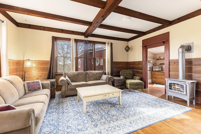 living area with wooden walls, light wood-type flooring, a wood stove, a wainscoted wall, and beamed ceiling