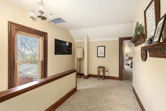hallway featuring light carpet, lofted ceiling, an inviting chandelier, and baseboards
