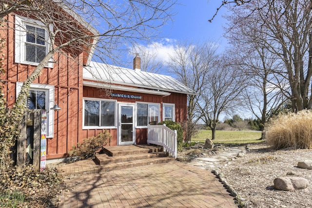 entrance to property with board and batten siding, a standing seam roof, a chimney, and metal roof