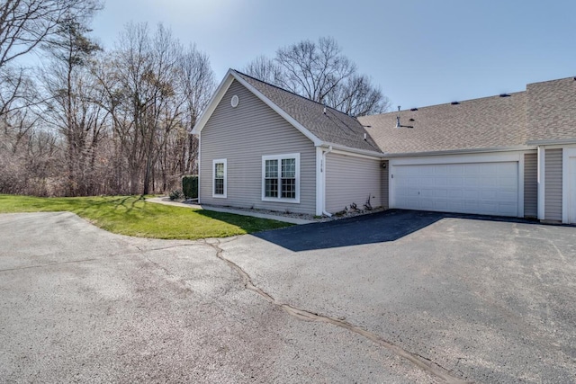 exterior space featuring an attached garage, a shingled roof, aphalt driveway, and a front yard