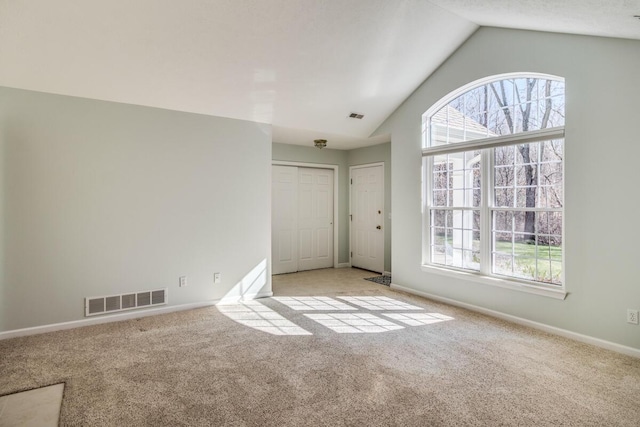 carpeted empty room featuring visible vents, a wealth of natural light, and lofted ceiling