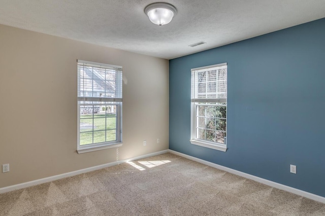 carpeted empty room featuring a textured ceiling, visible vents, baseboards, and plenty of natural light