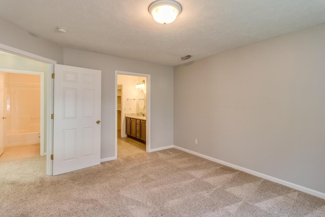 unfurnished bedroom featuring a textured ceiling, light colored carpet, baseboards, and ensuite bathroom