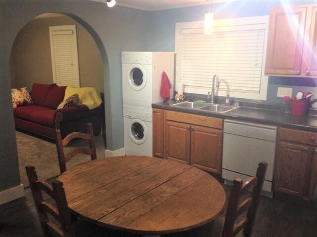 201 E Danaher St, Ludington, MI 49431 - kitchen featuring stacked washer and dryer, dark countertops, arched walkways, dishwasher, and a sink