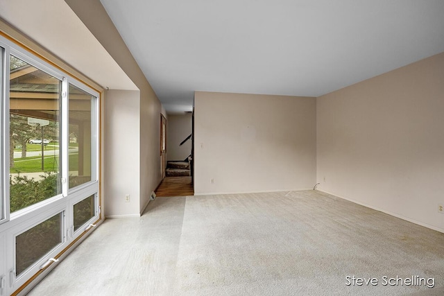 spare room with stairway, baseboards, and light carpet