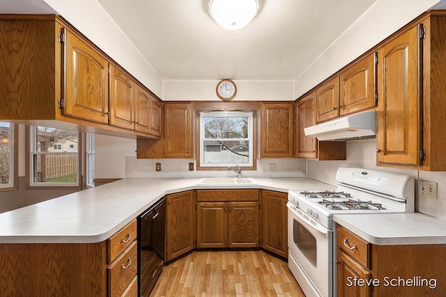 kitchen featuring white gas range oven, a sink, brown cabinetry, black dishwasher, and under cabinet range hood