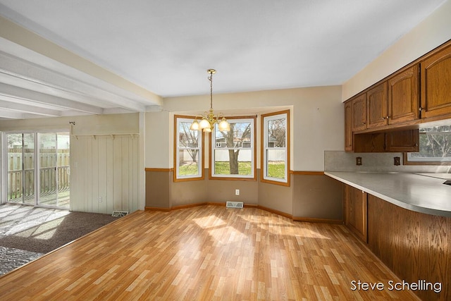 unfurnished dining area featuring light wood-style floors, a wealth of natural light, a notable chandelier, and visible vents