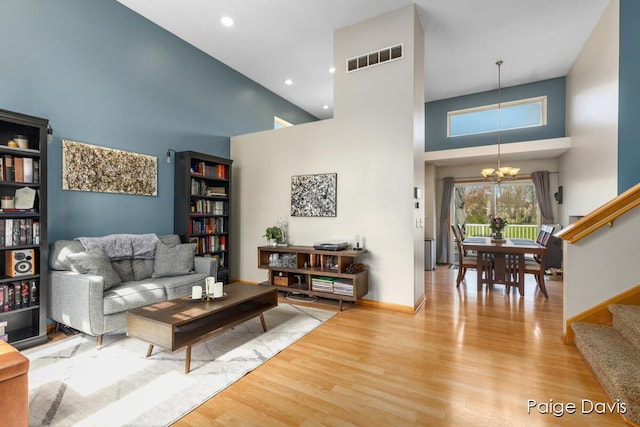 living room featuring stairs, visible vents, an inviting chandelier, and a towering ceiling
