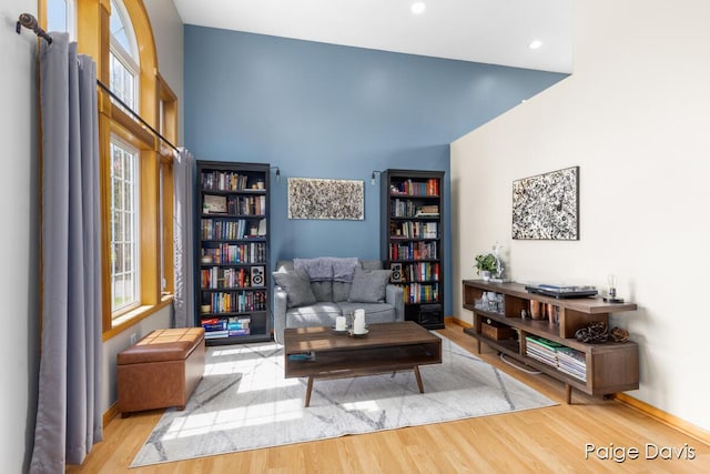 living area with recessed lighting, baseboards, wood finished floors, and a towering ceiling