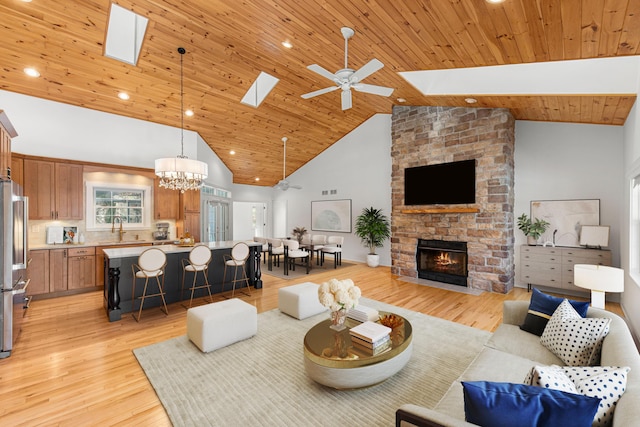 living area featuring ceiling fan with notable chandelier, high vaulted ceiling, a fireplace, a skylight, and light wood finished floors