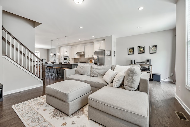 living room featuring dark wood finished floors, baseboards, visible vents, and stairs