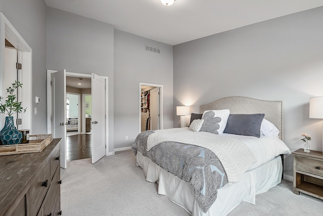 bedroom with visible vents, light carpet, a walk in closet, a closet, and baseboards