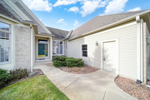 entrance to property with a shingled roof and brick siding