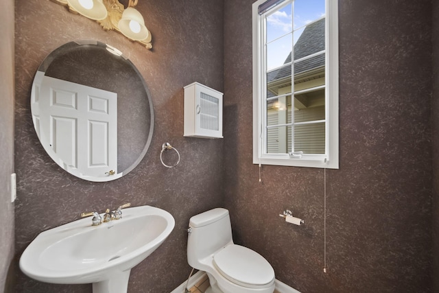 half bathroom with toilet, wallpapered walls, a sink, and baseboards