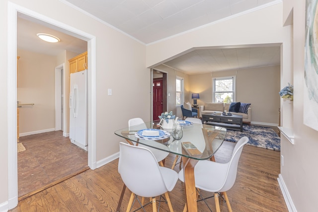 dining area with crown molding, baseboards, and light wood-type flooring