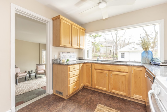 kitchen with dark stone counters, ceiling fan, stove, visible vents, and a sink