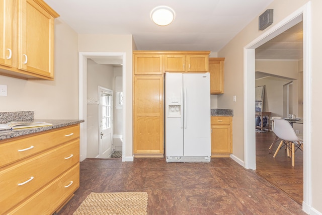 kitchen featuring white refrigerator with ice dispenser, dark stone counters, light brown cabinets, and baseboards