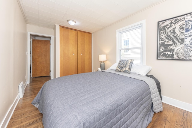 bedroom with crown molding, wood finished floors, baseboards, and a closet