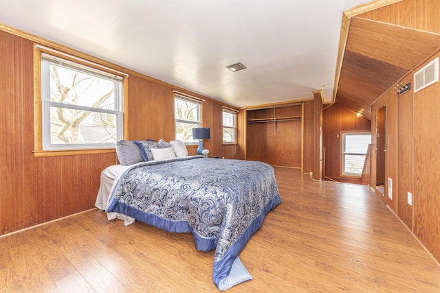bedroom featuring wood finished floors, wooden walls, a closet, and visible vents