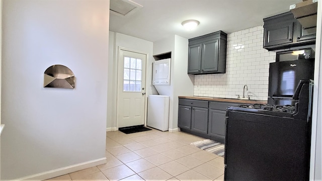 kitchen featuring light tile patterned floors, a sink, stacked washer and clothes dryer, gray cabinets, and backsplash
