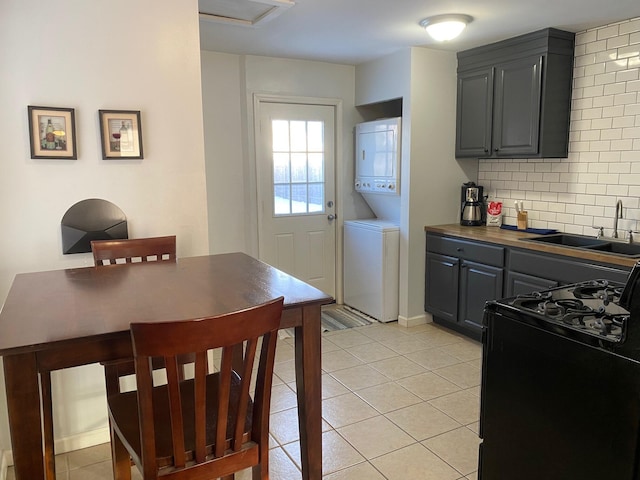 kitchen with tasteful backsplash, a sink, stacked washer and dryer, gas stove, and light tile patterned flooring