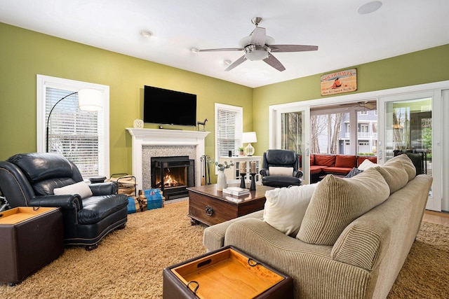 living area with wood finished floors, a ceiling fan, and a warm lit fireplace