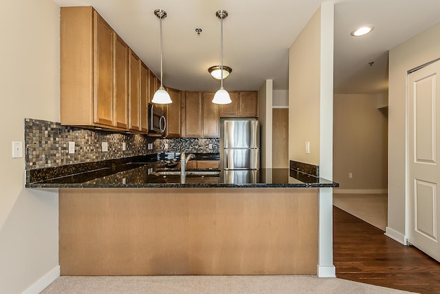 kitchen with stainless steel appliances, a peninsula, a sink, dark stone countertops, and tasteful backsplash